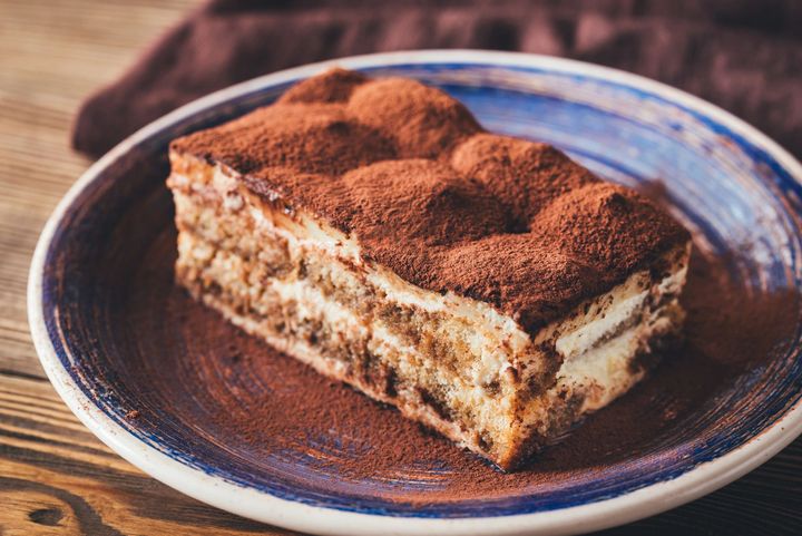 Una fetta di tiramisù su un piatto con il bordo blu e una spolverata di cacao.