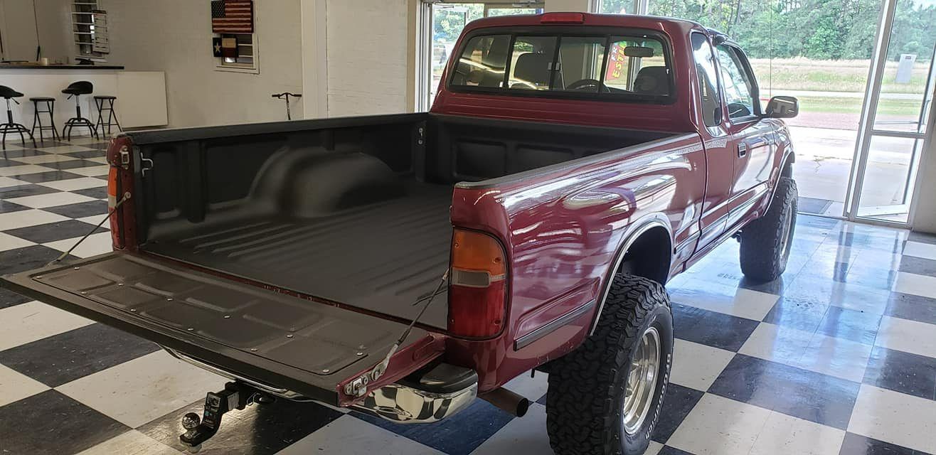A maroon pickup truck with its tailgate down, parked on a black and white checkered floor in a garage.