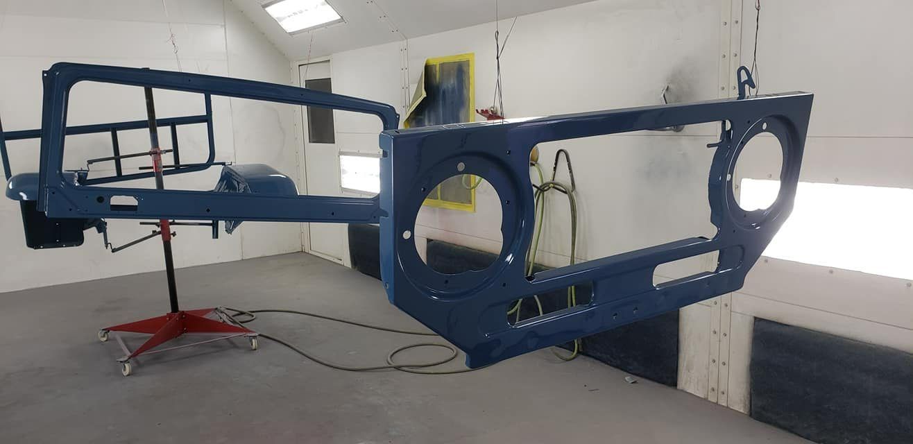 A blue painted vehicle front-end grille assembly hanging in an automotive spray booth.