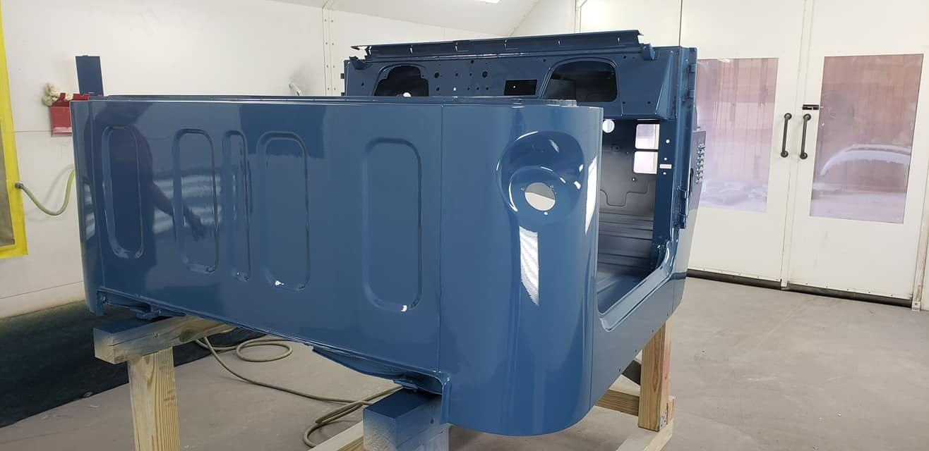A fresh blue paint job on the rear body shell of a vintage Jeep, mounted on wooden stands inside a workshop.