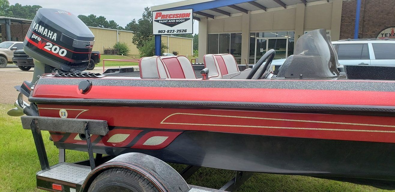 A red and black bass fishing boat with a Yamaha 200 outboard motor parked on a trailer in front of a building.