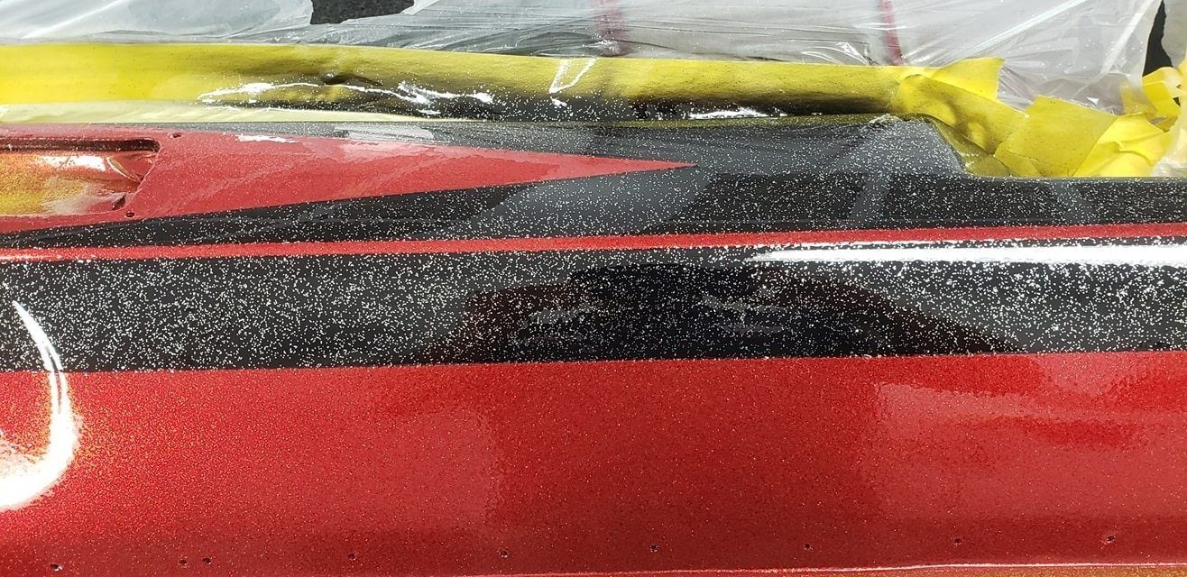 A close-up of a glossy, metallic red and black striped surface, likely a boat hull, with yellow masking tape visible.