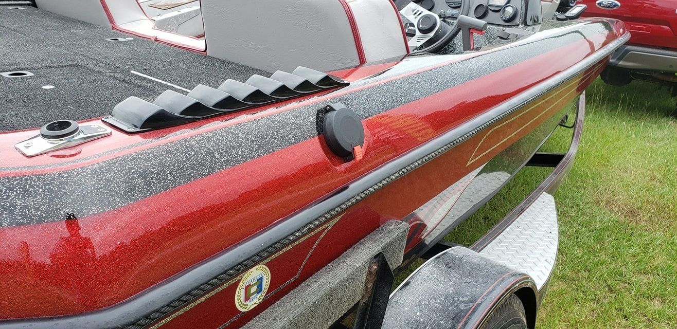 A close-up view of the side of a red and black speckled bass boat featuring rod storage clips and a circular outlet.