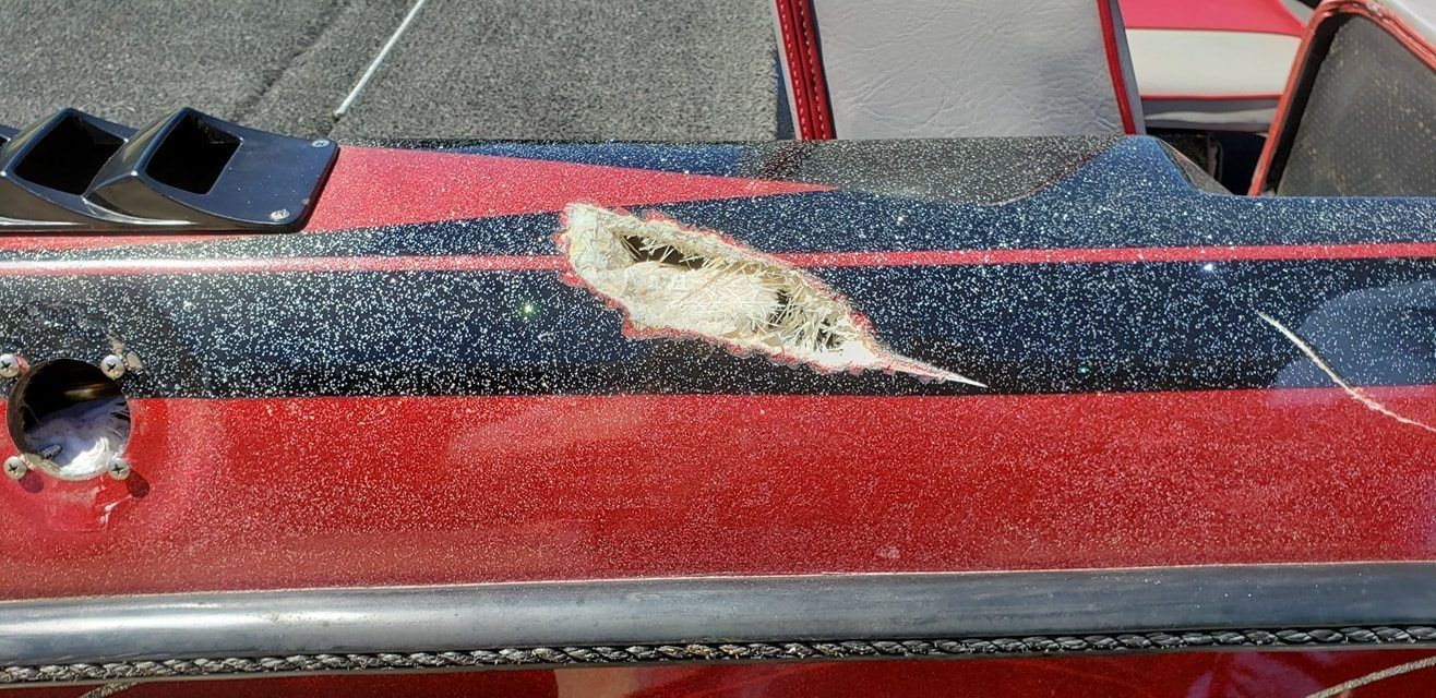 A close-up of a damaged fiberglass boat gunwale with exposed white material against a black-and-red glittery finish.