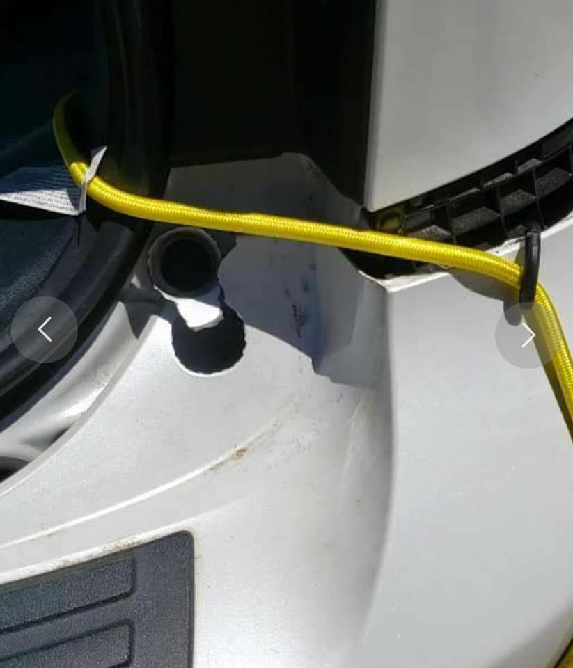 A yellow bungee cord is wrapped around a white vehicle's bumper and trunk latch area.