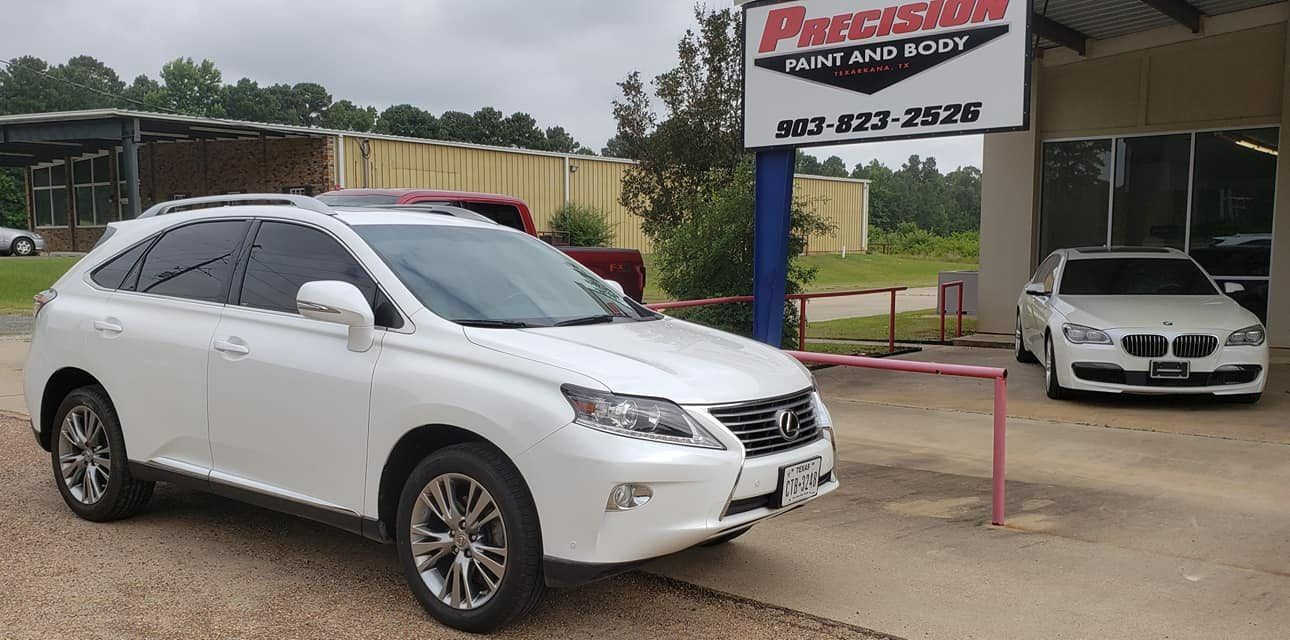 A white Lexus SUV parked in front of a Precision Paint and Body auto shop, with another white car visible in the garage.