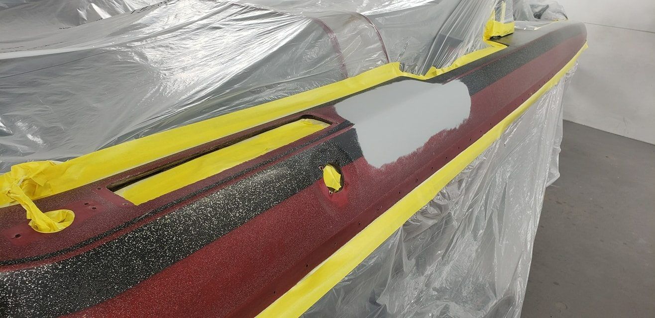 A boat gunwale prepared for repair, featuring a patch of grey filler, textured red non-skid surface, and yellow tape.