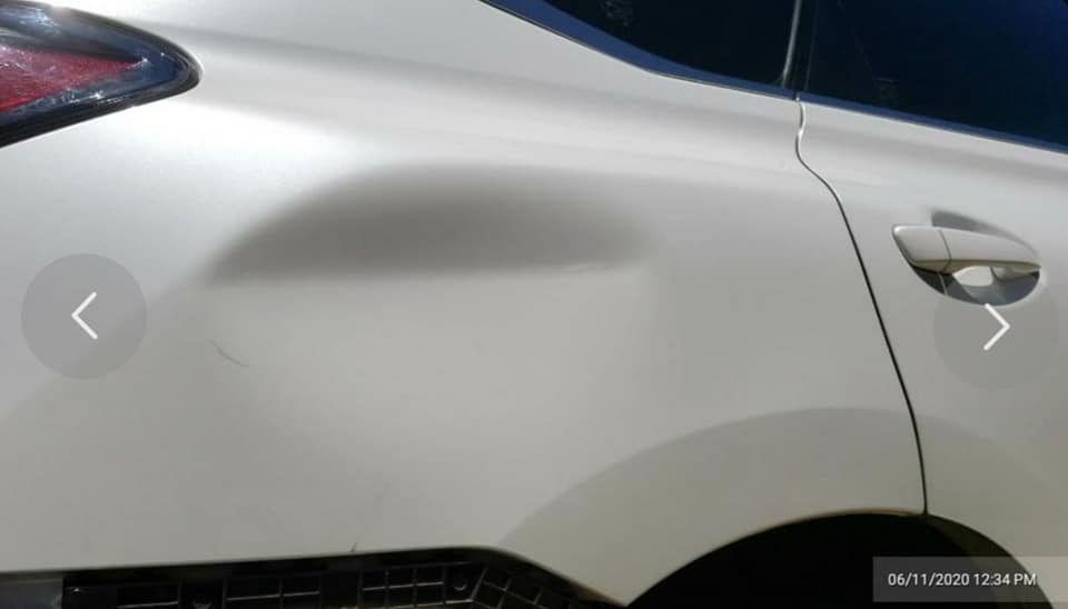 A white car with a large, smooth indentation on the rear quarter panel near the taillight.