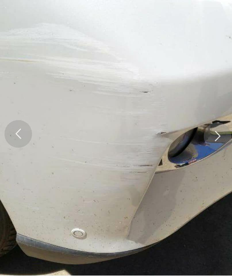 A close-up of a white car bumper showing superficial surface scuffs and paint transfer near the headlight.