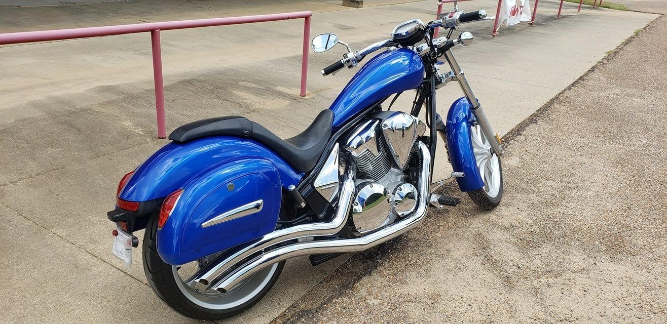 A glossy blue cruiser motorcycle parked on a paved surface next to a metal railing.