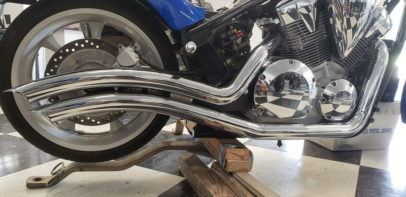 Side view of a blue cruiser motorcycle propped up on wooden blocks in a checkered-floor garage.
