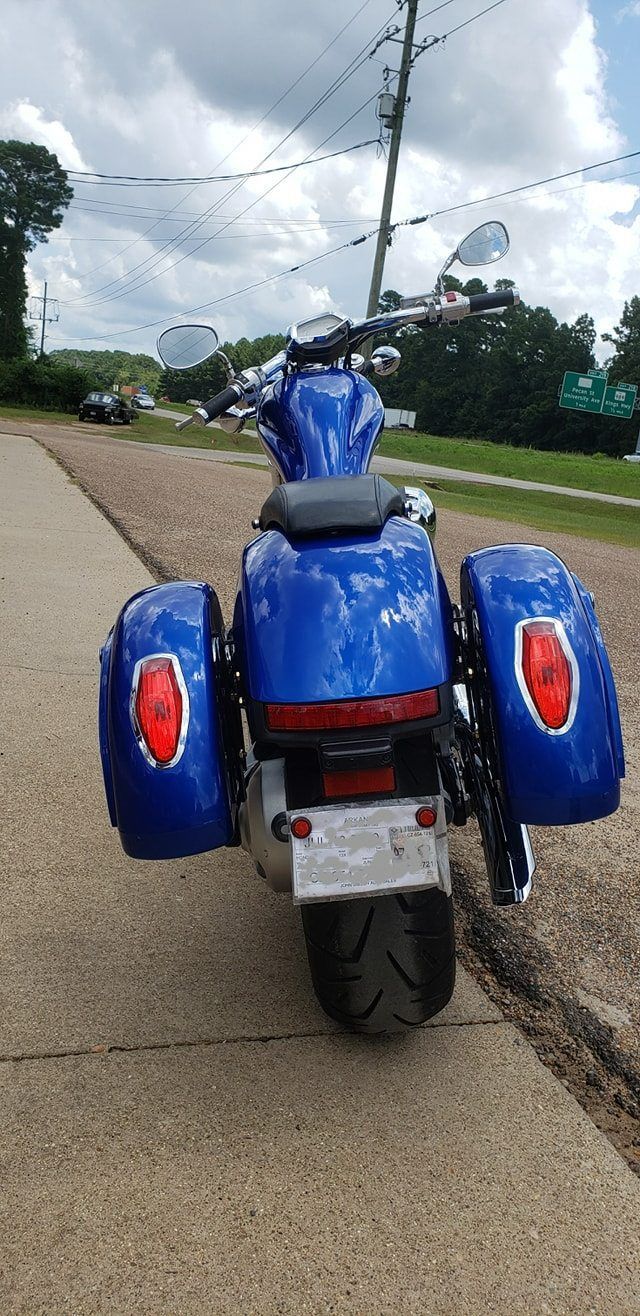 A bright blue motorcycle with hard saddlebags parked on a sidewalk on a cloudy day.