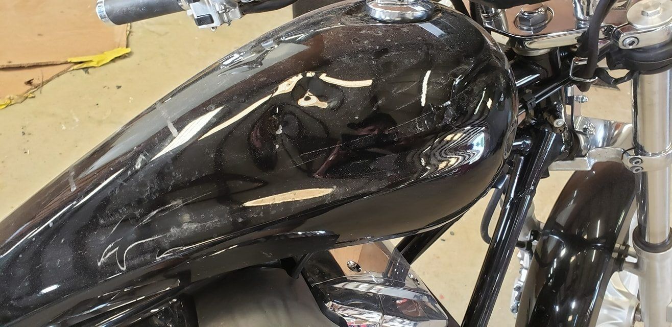 Close-up of a glossy black motorcycle fuel tank with metallic flake, captured in a garage setting.