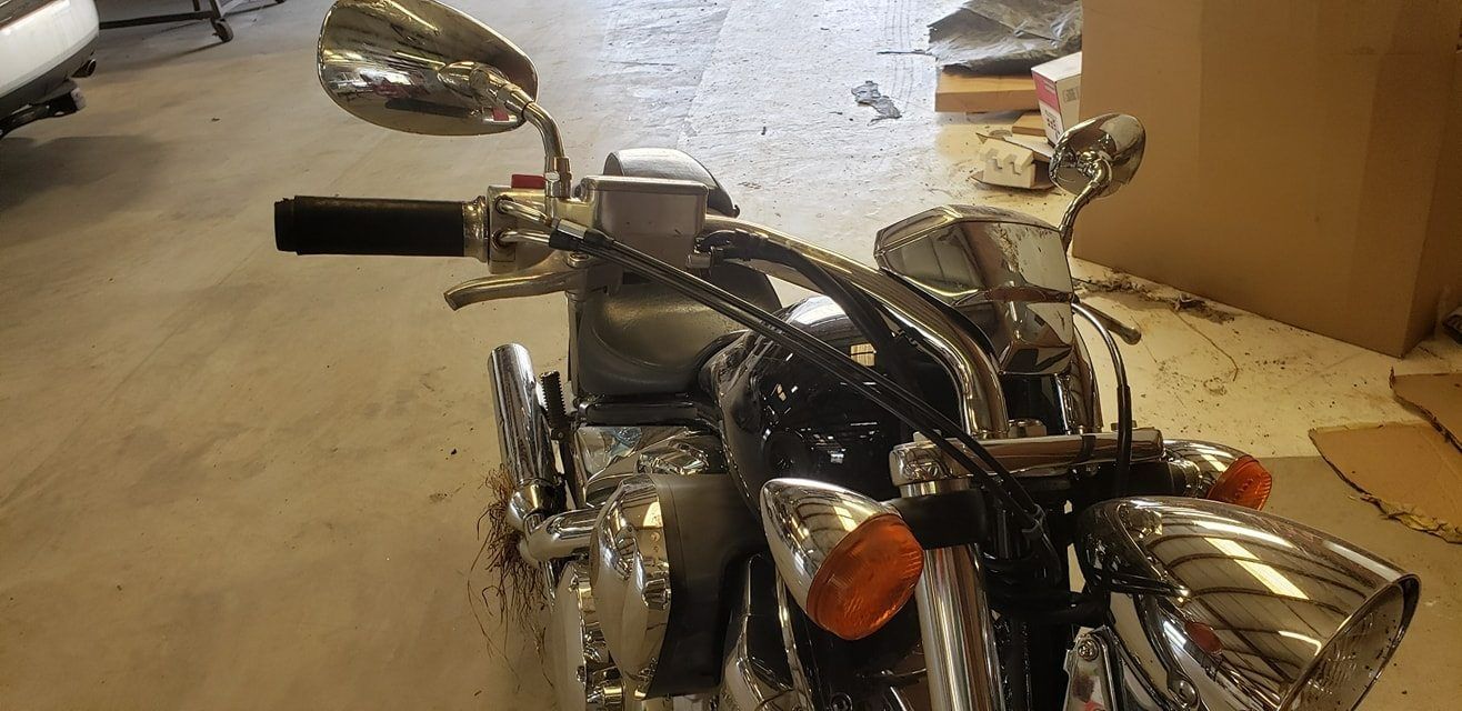 A high-angle view of a motorcycle's handlebars and chrome headlights, parked indoors on a concrete floor.