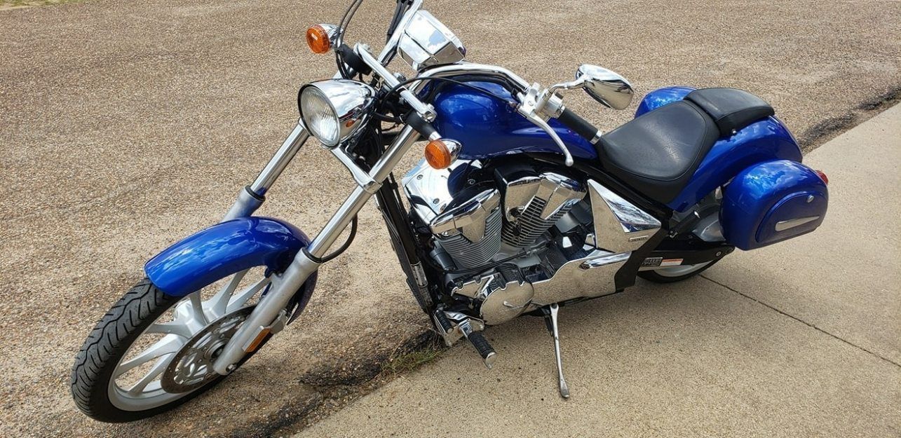 A blue cruiser-style motorcycle with chrome accents and hard saddlebags, parked on a paved surface.