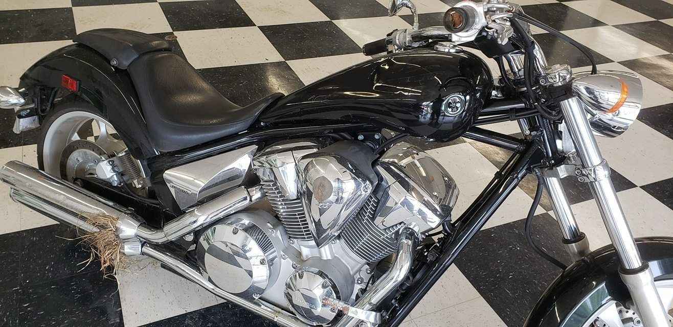 Black cruiser motorcycle with chrome engine components parked on a black and white checkered floor.