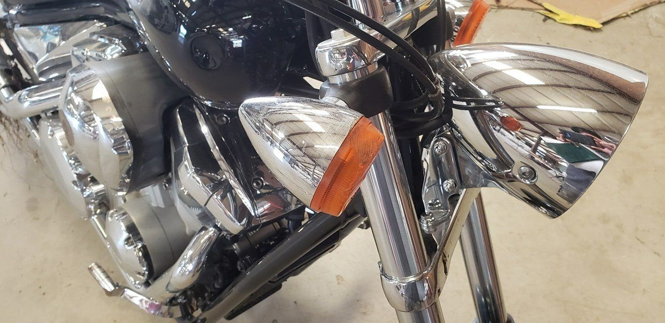 Close-up of a motorcycle's front chrome headlight and amber turn signal indicator.
