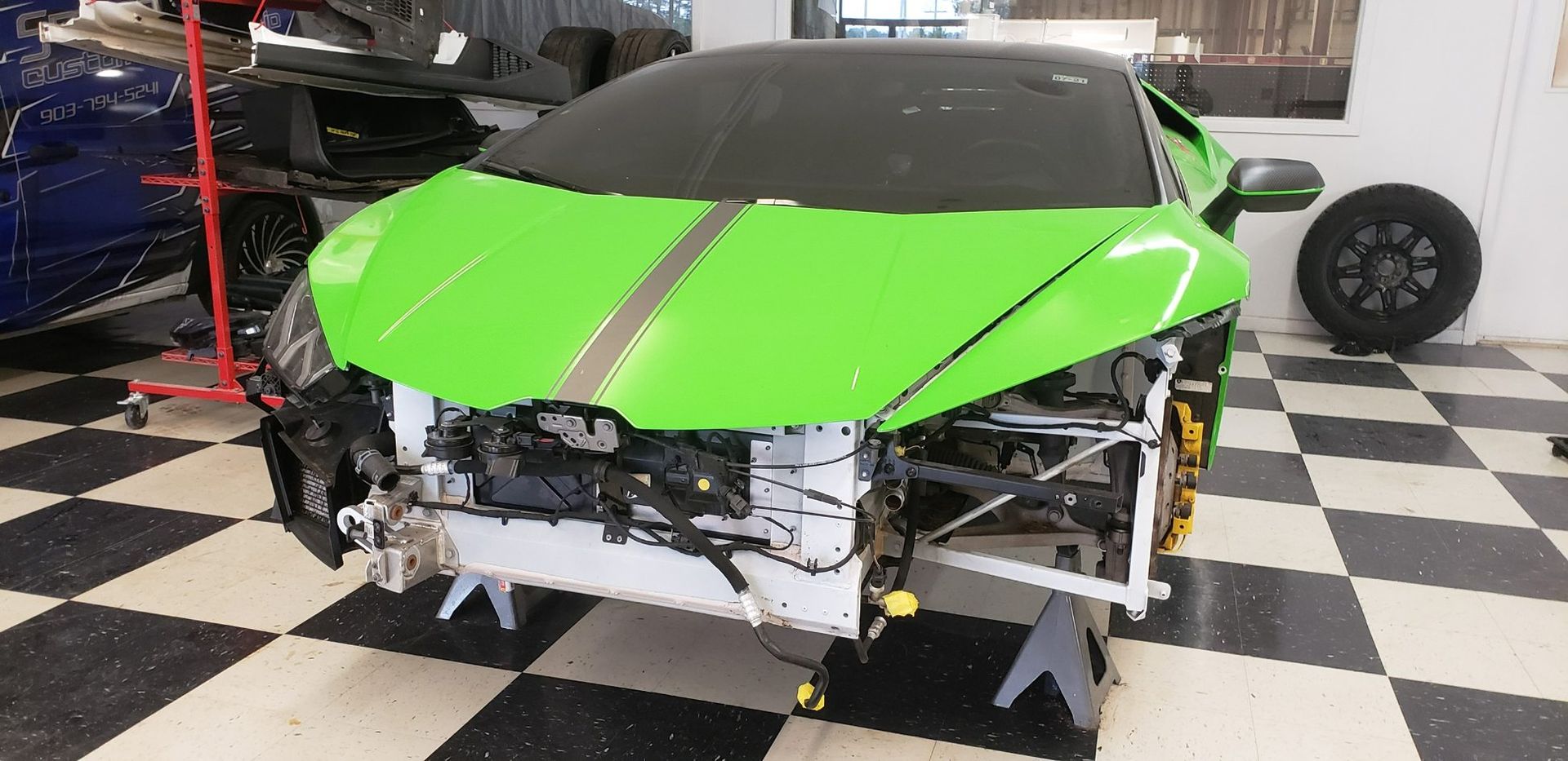 A lime green Lamborghini sports car undergoing repairs, missing its front bumper, resting on jack stands in a garage.