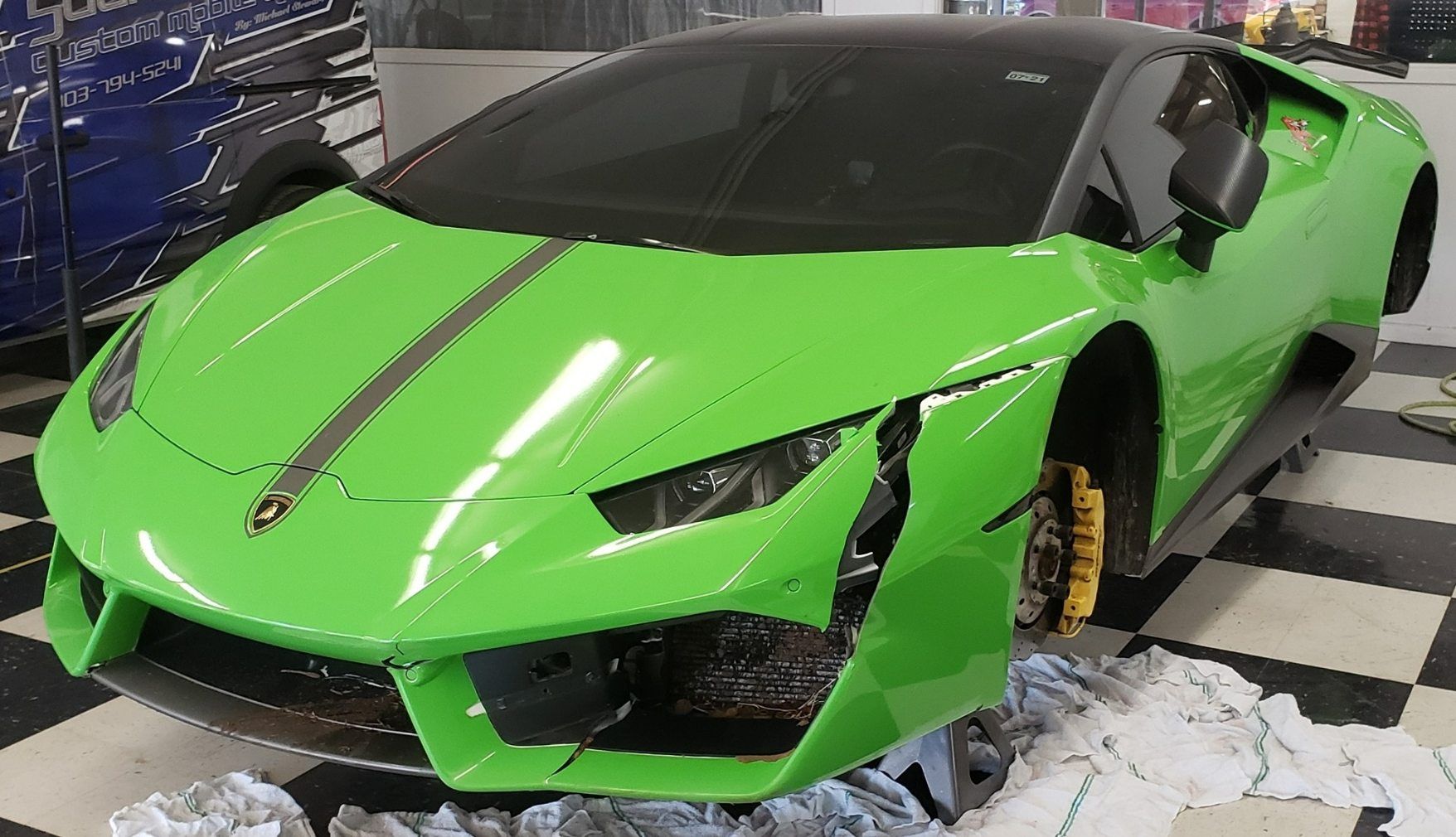 A damaged neon green Lamborghini sports car with a missing front wheel, undergoing repairs in a garage.
