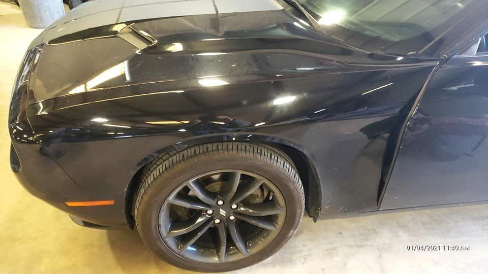 A close-up of a black Dodge Challenger showing the front fender, a dark wheel, and part of the hood.