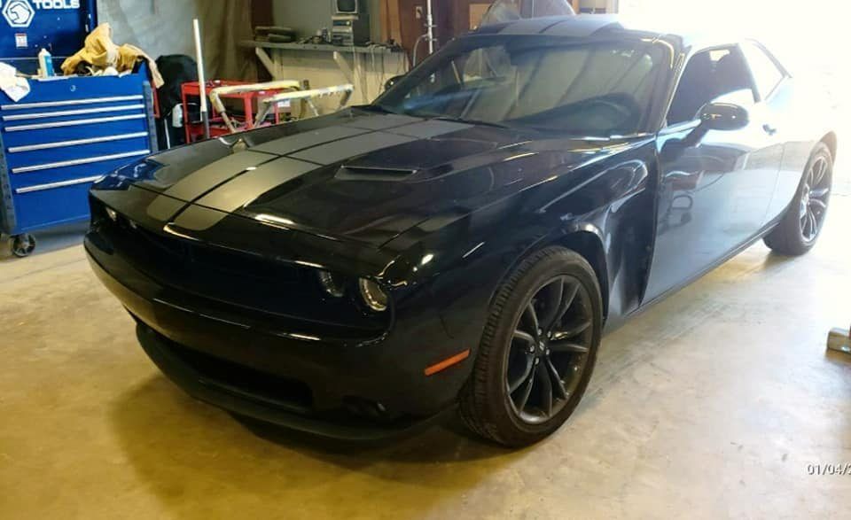 A black Dodge Challenger with racing stripes parked in a garage next to a blue tool chest.