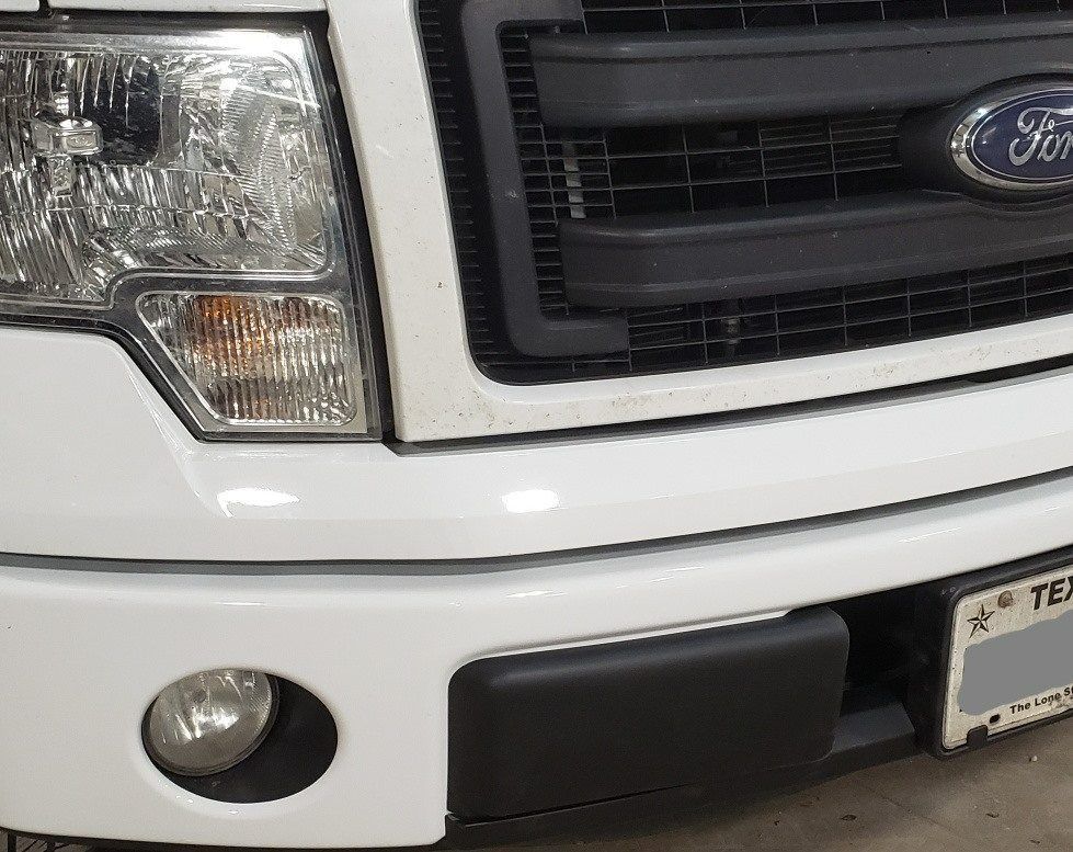 Front passenger-side view of a white Ford F-150 truck, showing the headlight, black grille, and front bumper.