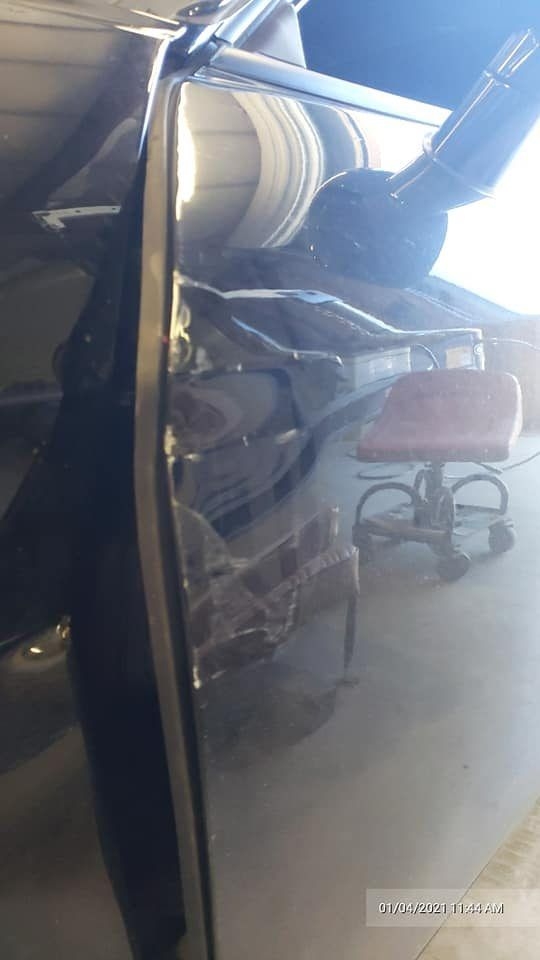 A reflective black car surface showing a distorted reflection of a rolling shop stool inside a garage.