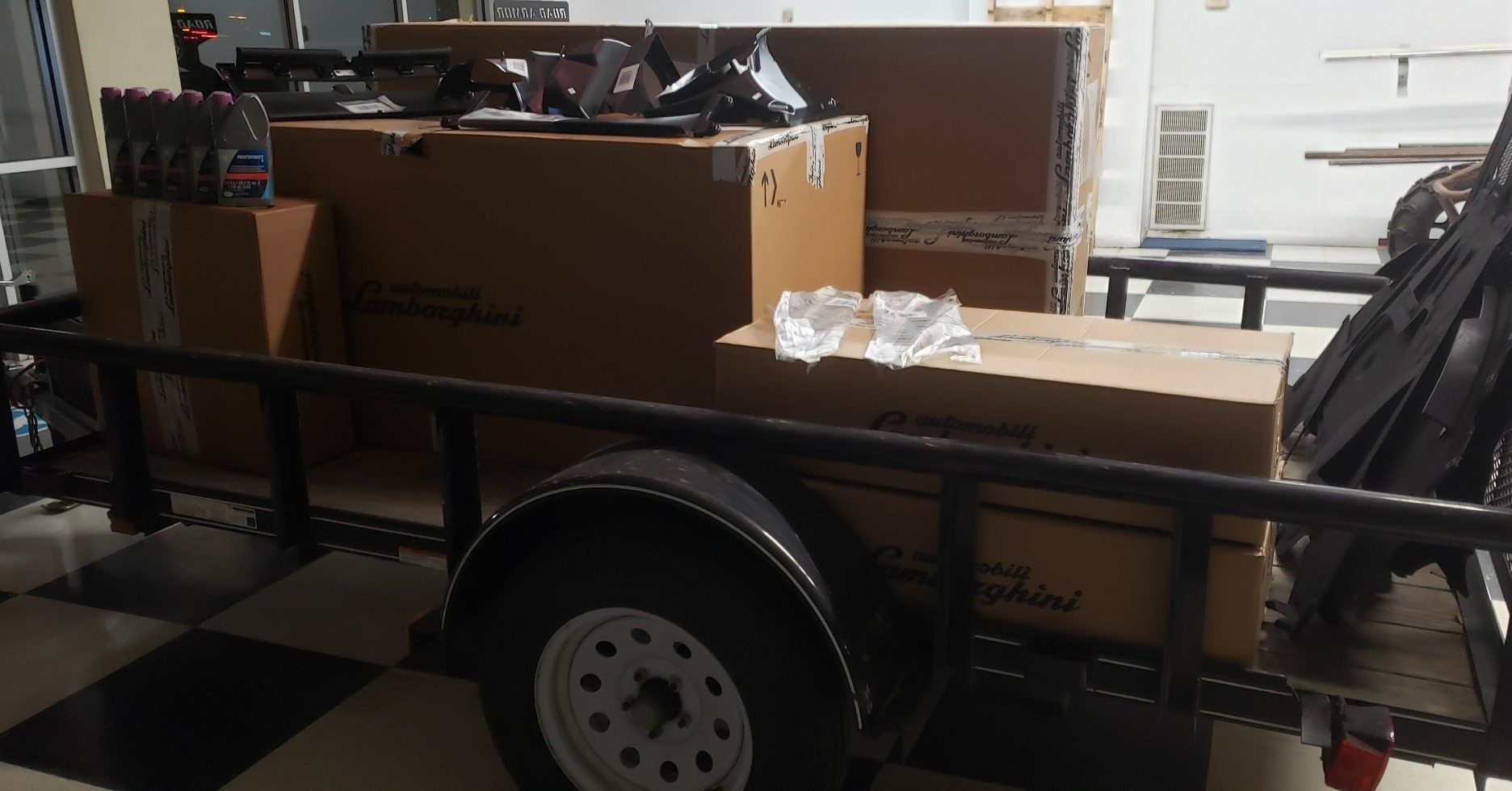 A utility trailer loaded with large cardboard boxes and various mechanical parts parked on a checkered floor.