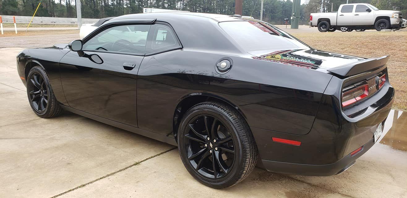 A sleek, black Dodge Challenger parked on a concrete lot with a white pickup truck in the background.