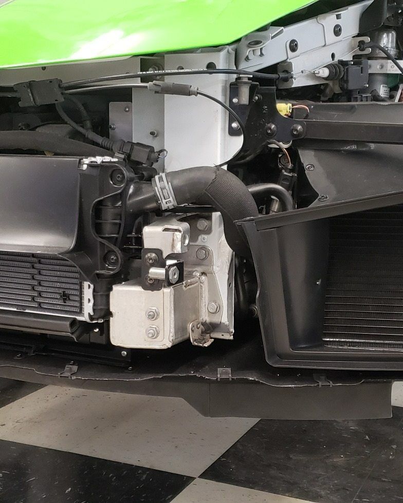 The front bumper of a lime green car is removed, revealing the radiator, structural frame, and black air intake ducting.
