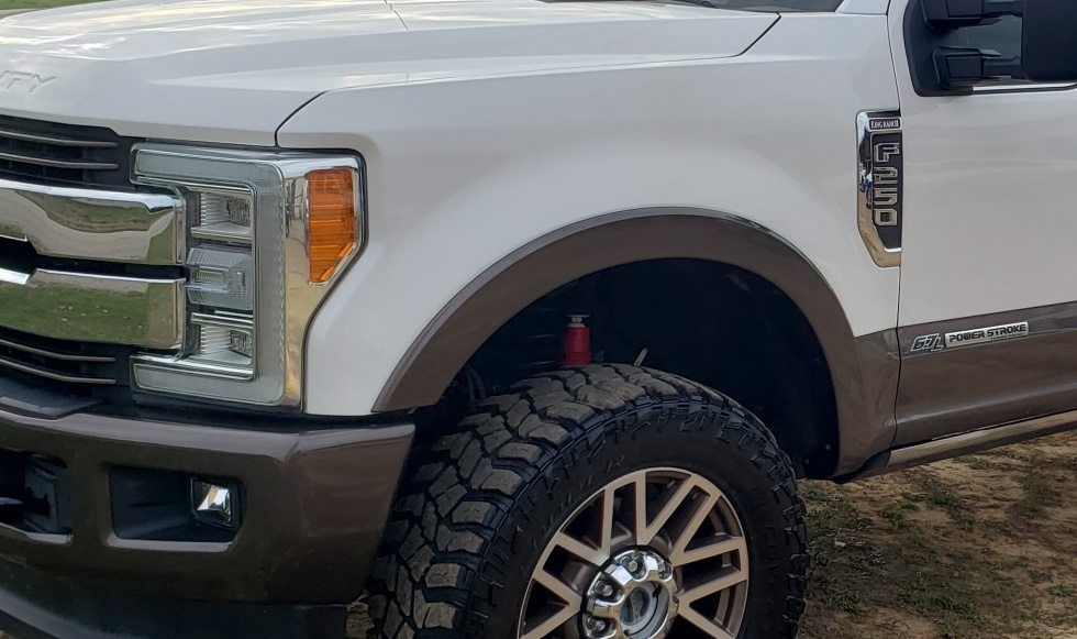 A white Ford F-250 pickup truck with brown trim, seen from the front passenger side, parked on dirt.
