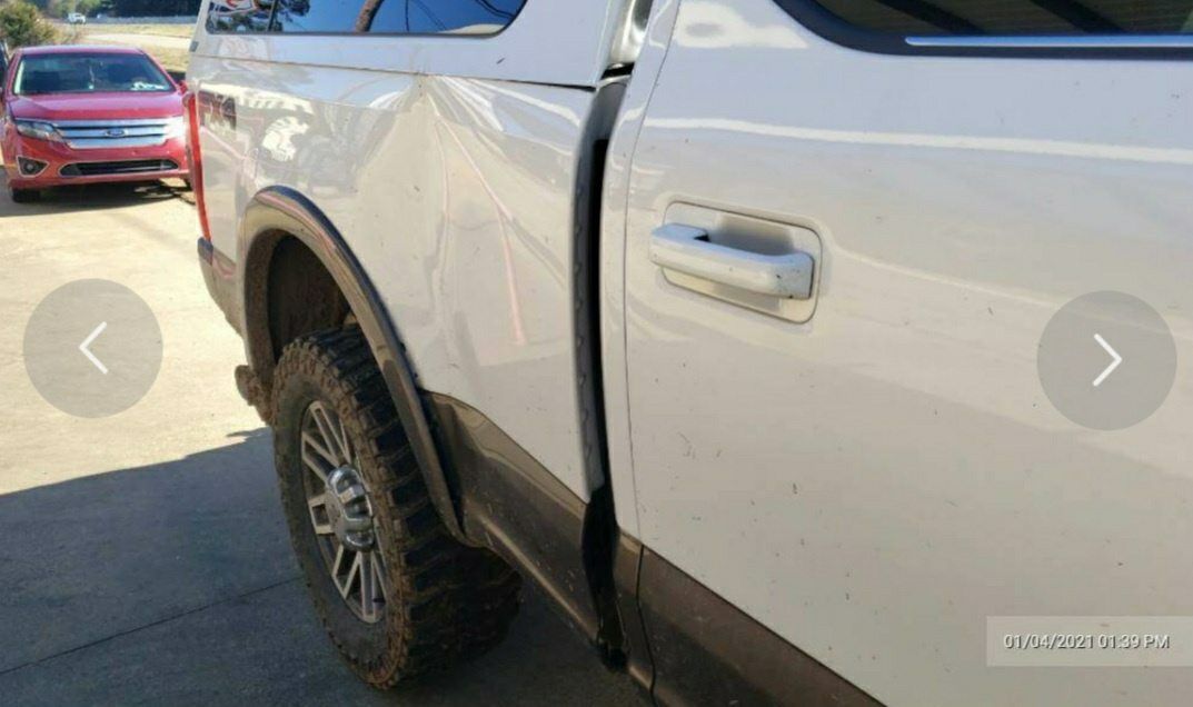 A side view of a white pickup truck showing a visible dent in the rear passenger-side body panel.