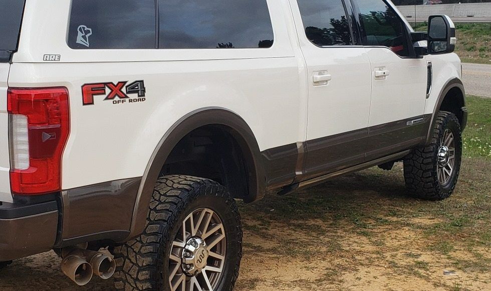 A white Ford Super Duty truck with an FX4 badge and two-tone brown lower trim parked on a dirt lot.