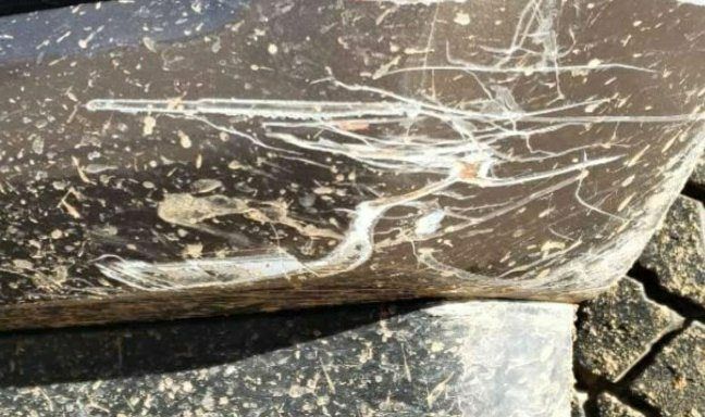 Deep, white scratches and mud splatter on the dark-colored bumper of a vehicle.