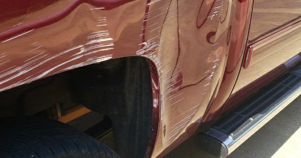 Close-up of a maroon truck's rear fender showing significant denting, scuff marks, and paint damage.