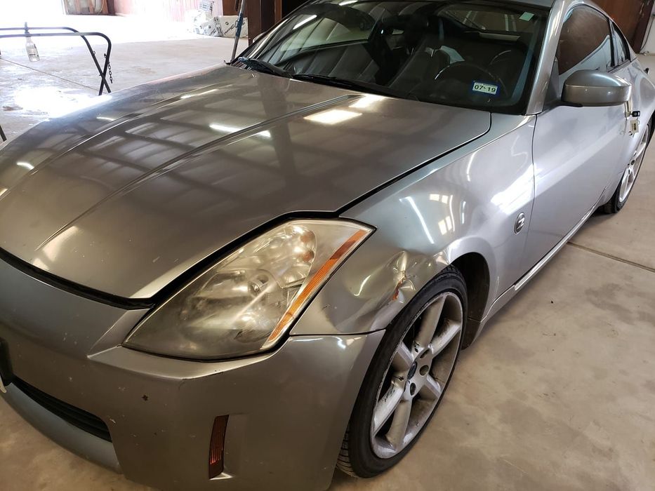 A silver Nissan 350Z parked in a garage, showing minor body damage to the front driver-side fender.
