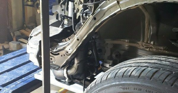 A close-up view of the front quarter panel of a car undergoing repair in a garage, revealing the internal frame structure.
