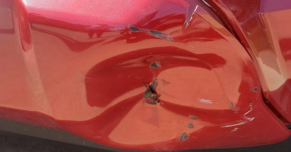 A close-up of a deep dent and chipped paint on a shiny red car body panel.