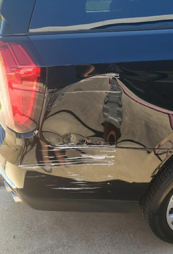 A black car’s rear quarter panel shows paint scrapes and a dent below the taillight.