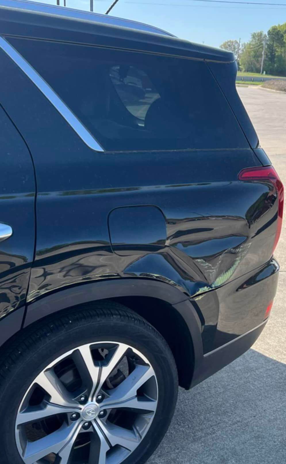 A close-up view of the rear quarter panel of a black SUV showing damage and denting near the fuel door and wheel well.