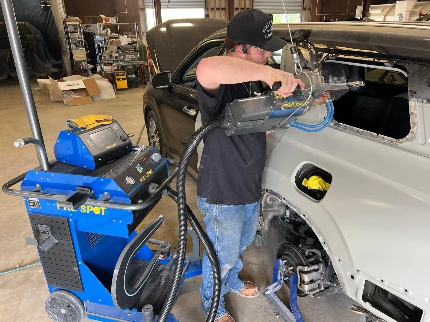 A technician uses a Pro Spot welder on a car's rear quarter panel in an auto repair shop.