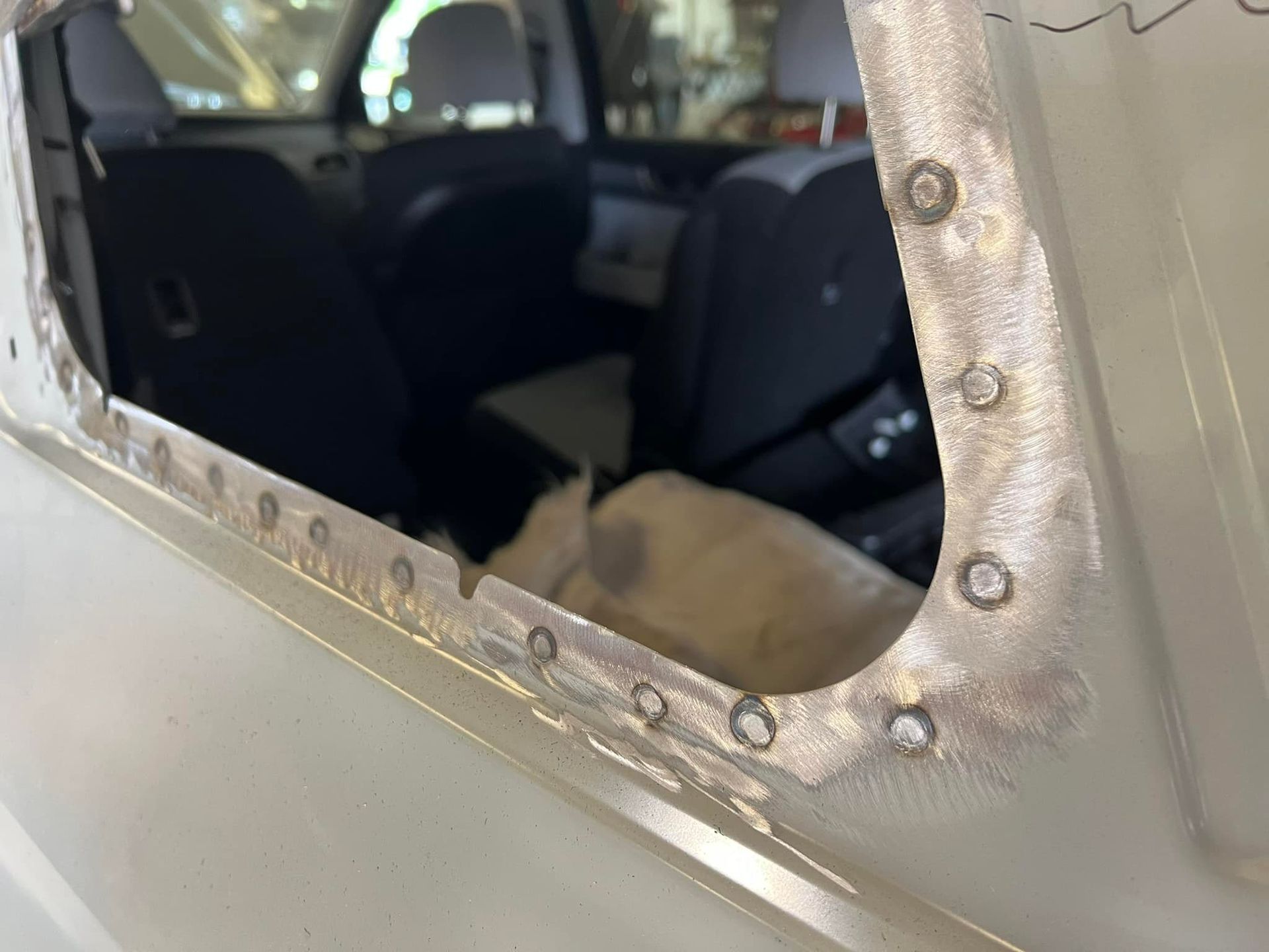 A close-up view of a car window frame showing a line of spot welds along the metal edge where a panel has been repaired.