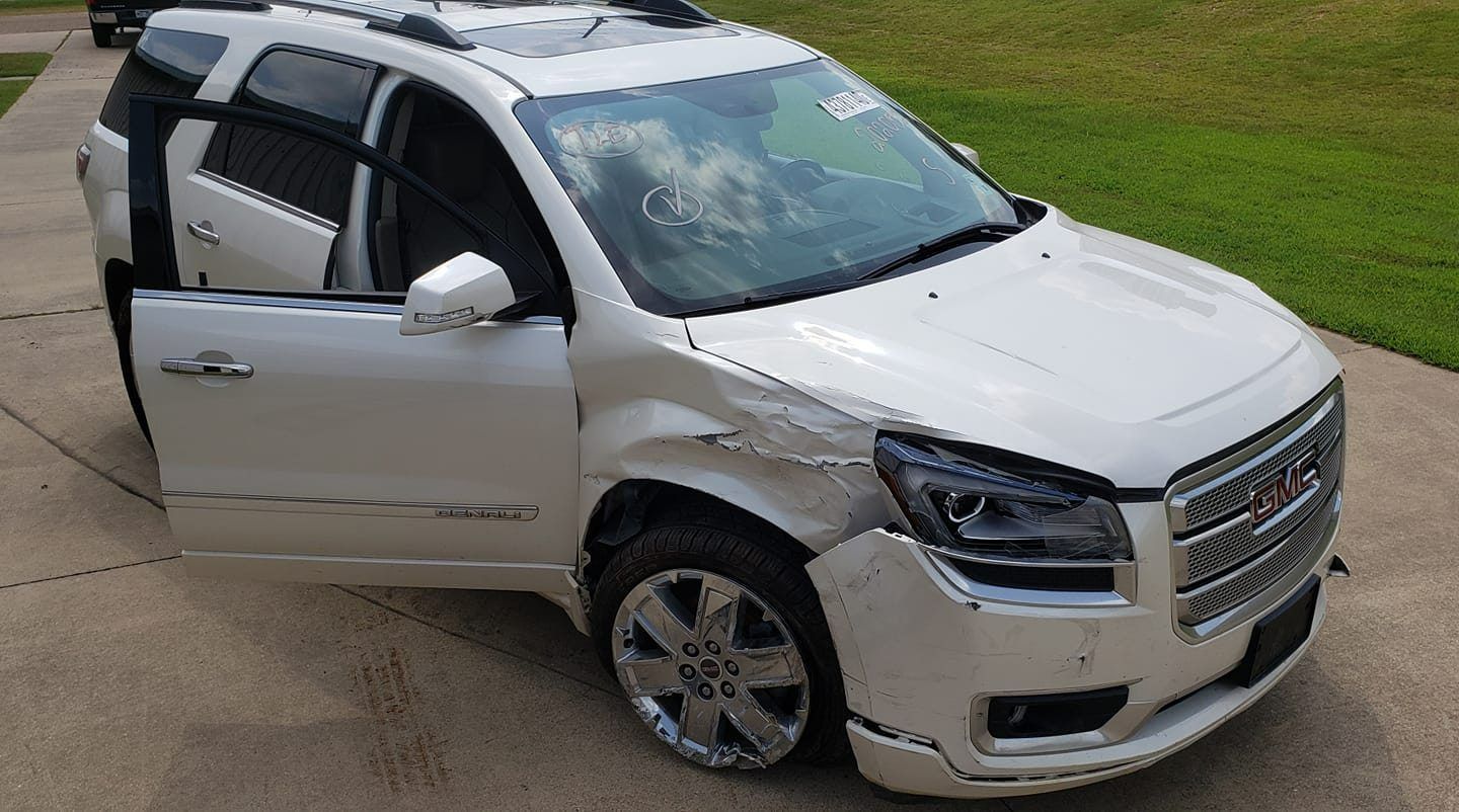 A white GMC SUV with heavy front-end and passenger-side body damage parked on a concrete driveway.