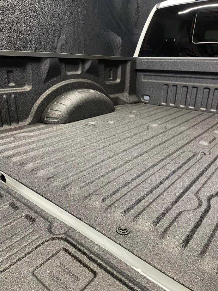 A black spray-in bed liner covering the interior of a truck bed, highlighting the textured surface and wheel wells.