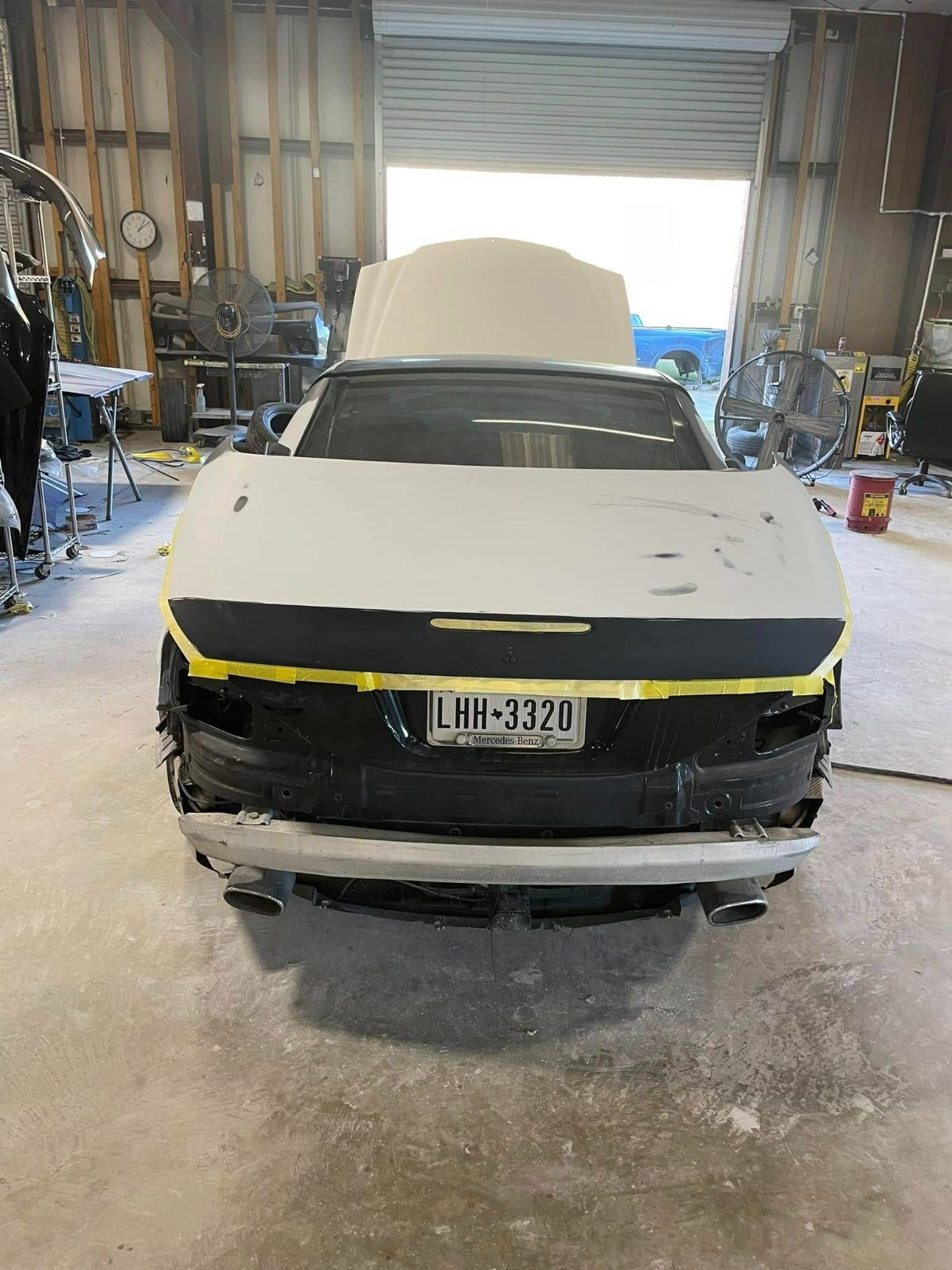 A car undergoing auto body repair in a shop, with a gray primer-coated trunk lid and exposed rear components.