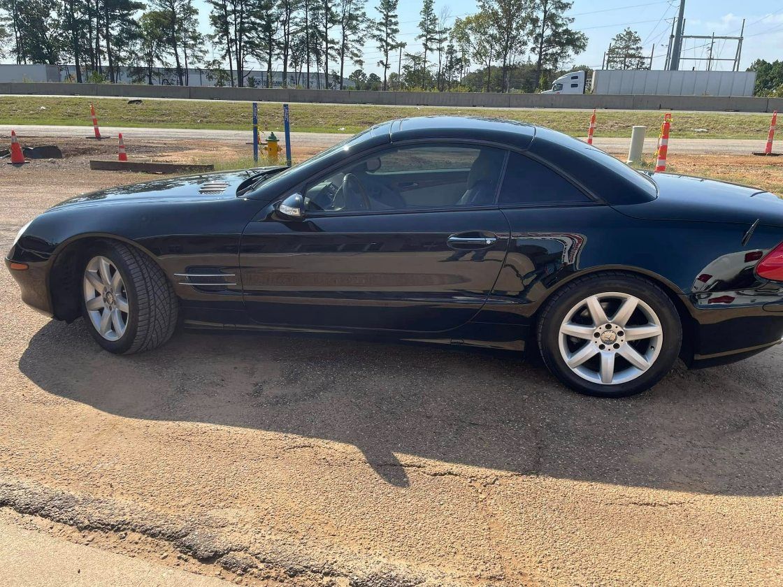 A black Mercedes-Benz SL-Class convertible parked on a dirt lot on a sunny day.