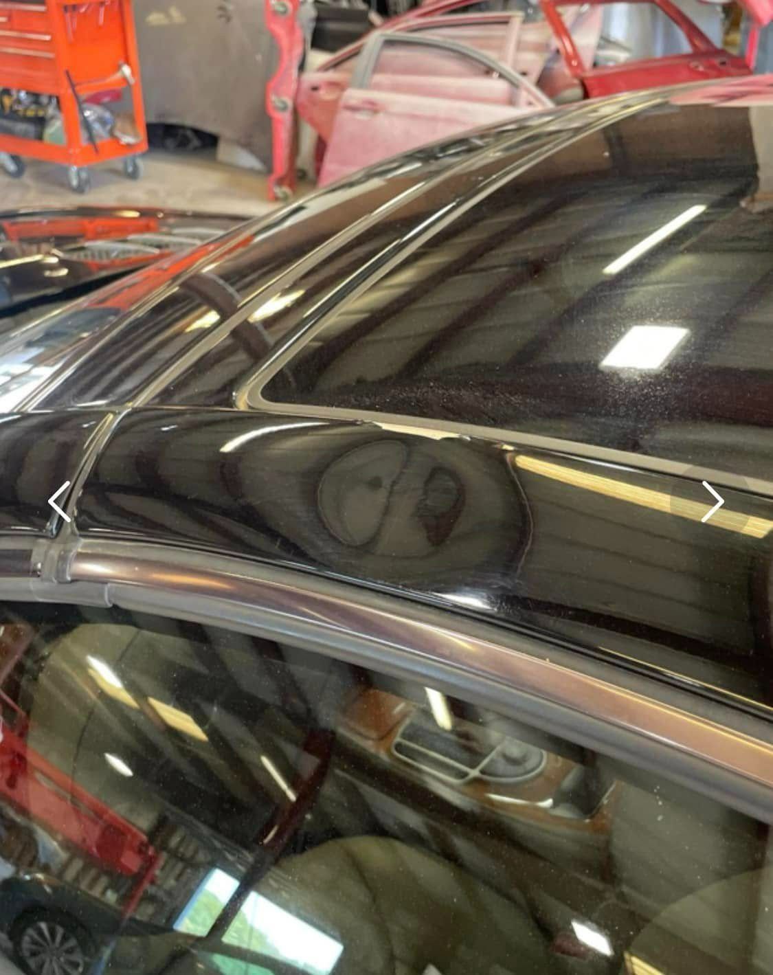A close-up view of a car roof, focusing on the trim and the edge of a panoramic sunroof in a workshop setting.