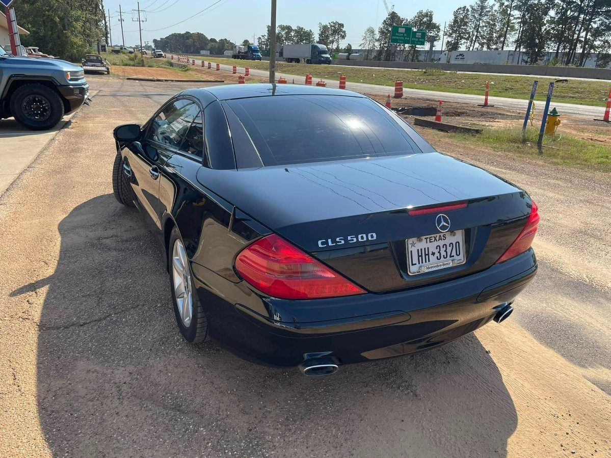 A black Mercedes-Benz CL-Class coupe parked on a gravel shoulder near a highway underpass.