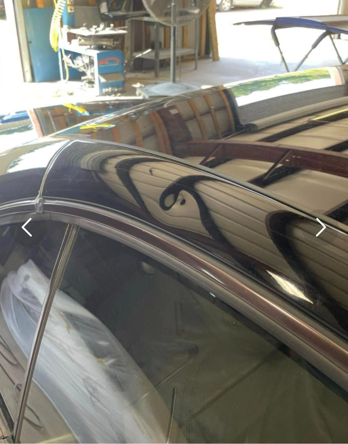 Close-up view of a car's curved window frame with black tribal-style decals, inside a workshop.