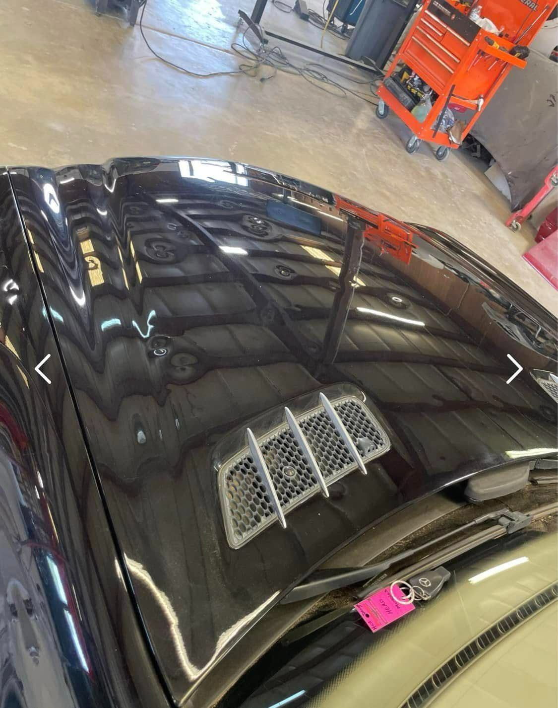 A glossy black car hood with a silver-mesh air vent, viewed from a high angle inside a workshop.